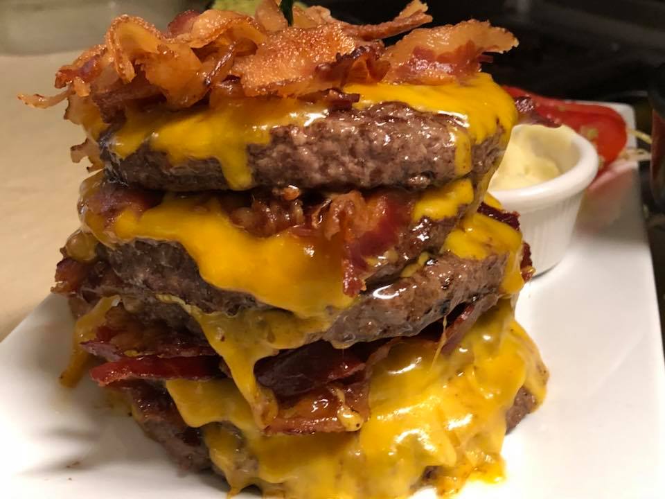 Three juicy burgers stacked on top of each other are loaded with melted cheese and bacon