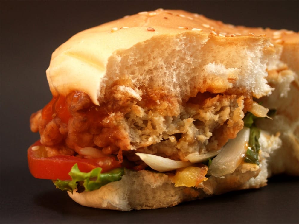 A delicious chicken burger topped with sauce, lettuce, tomato and onion