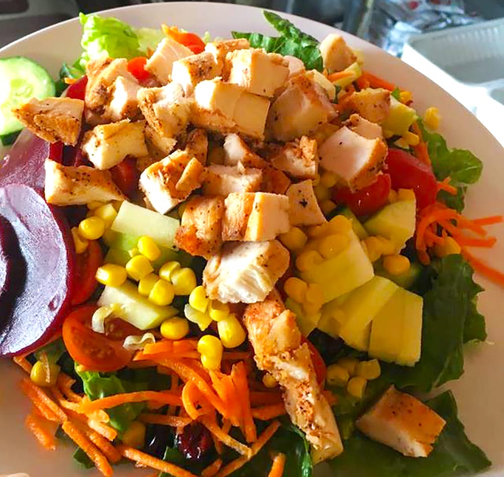 A large green salad with chicken, beets, zucchini, carrots, tomatoes, corn and more