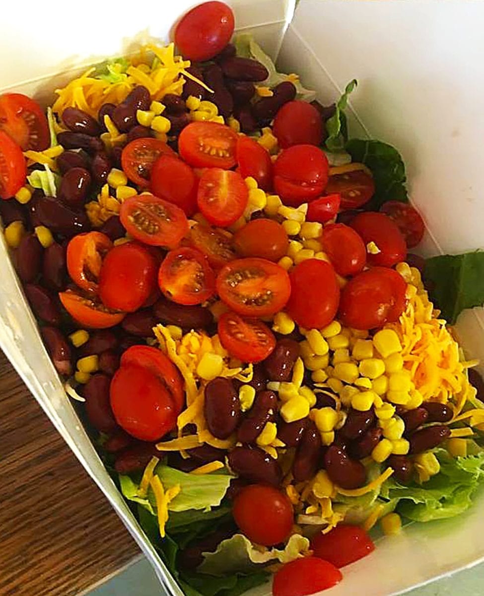 A to go salad with greens, black beans, corn, cheese, cherry tomatoes and more