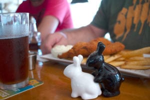 A plate of freshly cooked chicken tender and French fries sits in the foreground with a close-up of black and white bunnies salt and pepper shaker